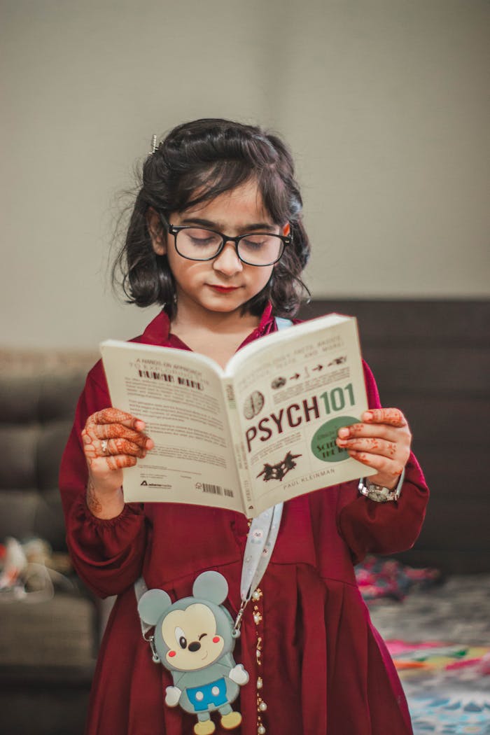 A young girl reading a Psych 101 book indoors, showcasing cultural attire and curiosity.