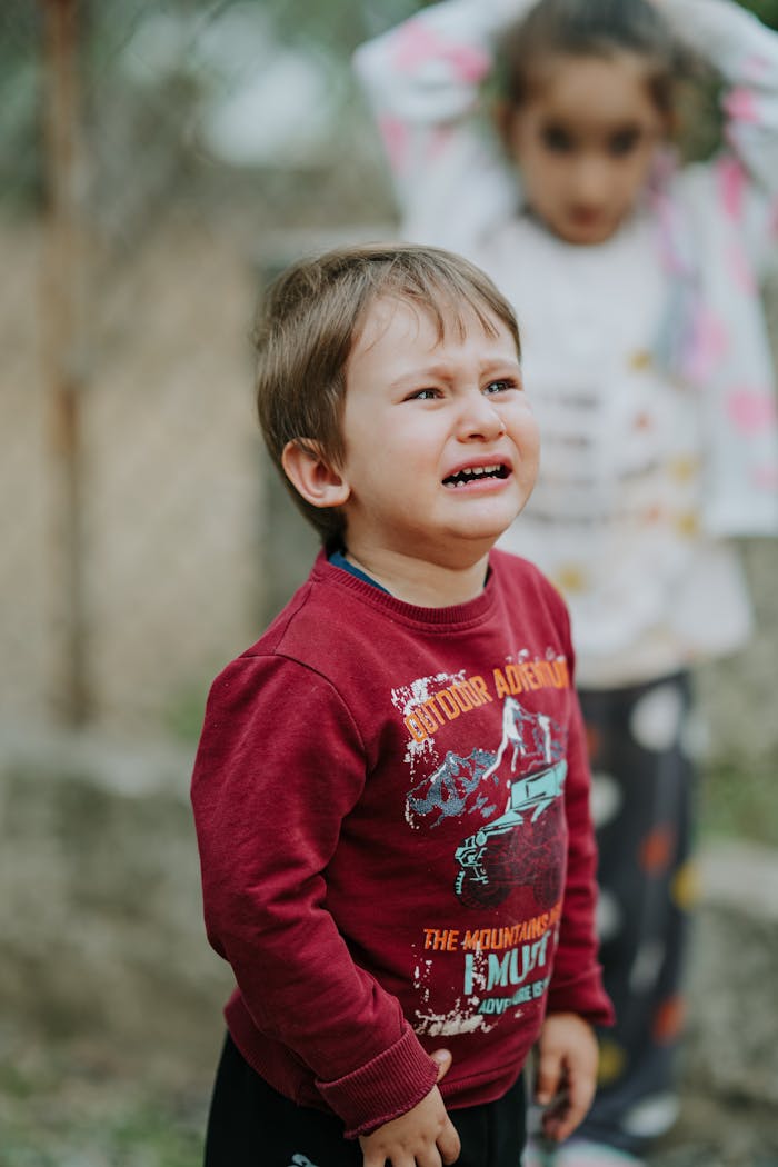 A young child crying outdoors, wearing a casual sweater, expressing sadness.