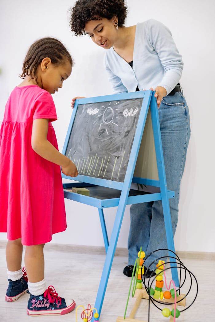 A young girl and teacher enjoy a creative learning session with a blackboard indoors.